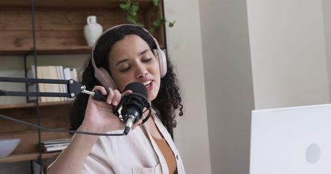 African american woman recording podcast at home desk with headphones and microphone