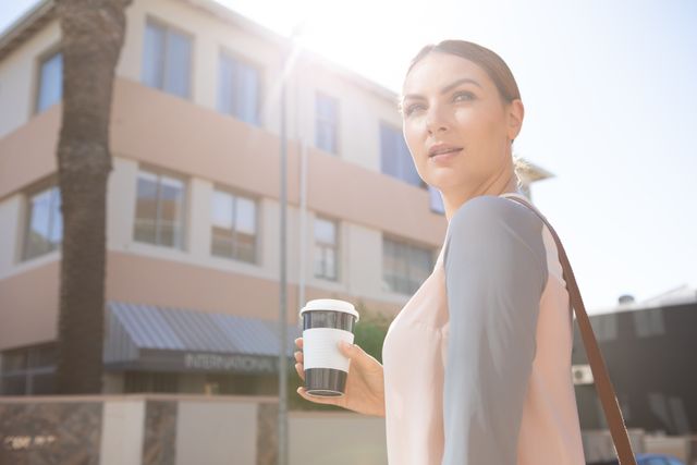 Caucasian businesswoman walking in city street holding a takeaway coffee cup. Ideal for use in business, career, and lifestyle contexts, showcasing modern professional life, urban living, and on-the-go work habits.