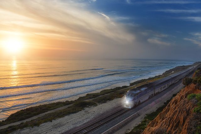 Train traveling on a scenic coastal railway with cliffs and ocean views during a beautiful sunset. Ideal for travel promotions, transportation themes, environmental awareness, and tourism materials highlighting scenic routes and coastal beauty.
