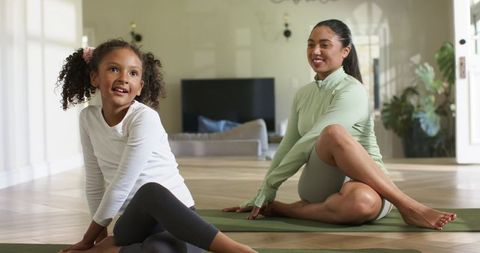 Mother and daughter practicing seated twist yoga together in sunlit living room