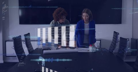 Coworkers leaning over plans reviewing holographic data overlays in modern sleek boardroom