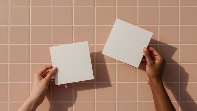 Hands holding white cards against peach tiled background