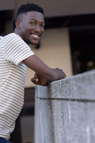 Young man leaning on concrete wall smiling and meeting gaze on urban balcony