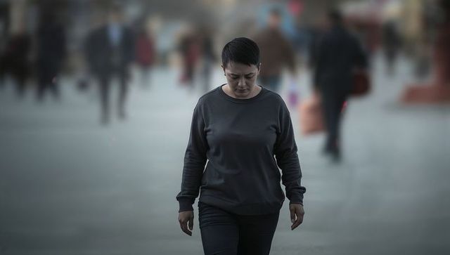 Solitary woman walking through blurred urban plaza in dark pullover, contemplative mood