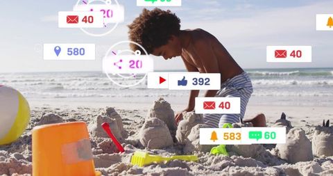 Boy building sandcastle while social media notifications float over sunny beach