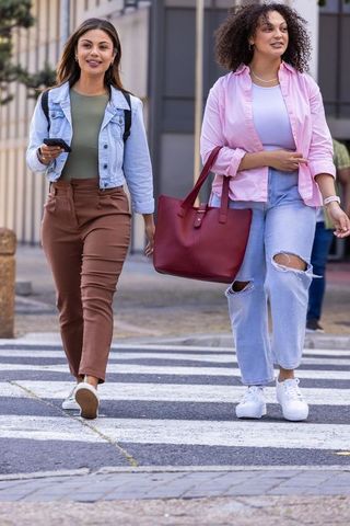 African american friends walking across city crosswalk carrying tote and phone
