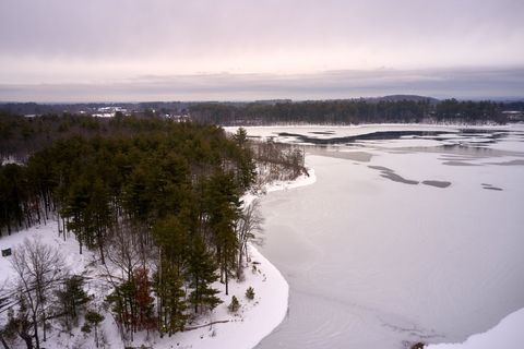 Ethereal winter dawn over partially frozen lake and snow-covered pine peninsula