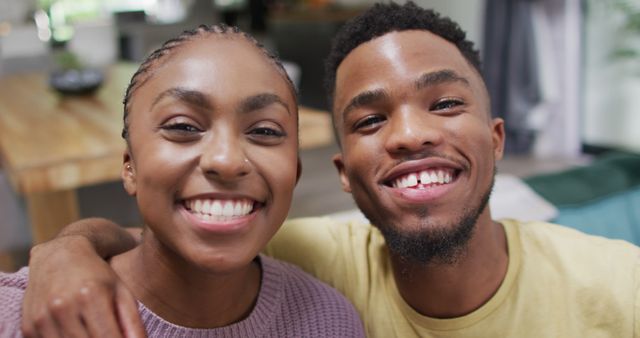Young African American couple smiling and posing indoors. Perfect for promoting relationships, friendship, and family unity. Can be used in advertisements, social media posts, and articles focusing on love, happiness, and togetherness.