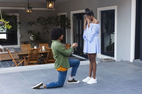 African american man proposing on one knee surprising partner on terrace engagement