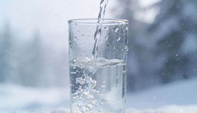 Pouring crystal clear water into tall glass against snowy forest backdrop, refreshing