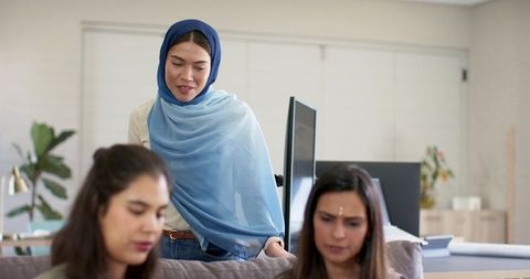Multicultural female team collaborating in modern office with woman wearing blue hijab