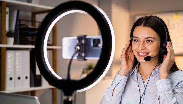 Remote customer service agent recording tutorial with ring light and headset in office