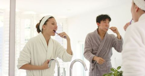Couple brushing teeth together in sunlit minimalist bathroom wearing robes at double sink