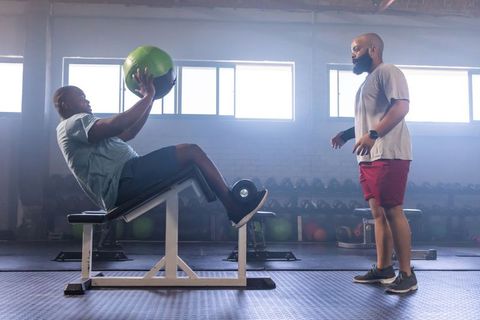 African american trainer coaching client doing medicine ball core twists on incline bench