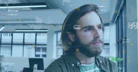 Bearded man studying augmented reality data overlays in modern open office workspace