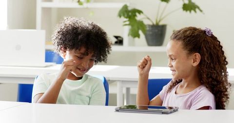 African American children celebrating using tablet in bright classroom learning together
