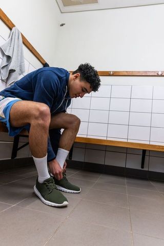 Male athlete tying running shoes on bench in locker room preparing for workout