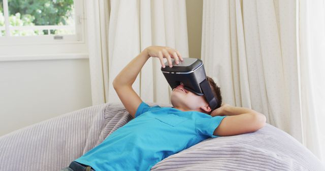 Young boy lying on a bean bag, immersed in virtual reality experience using a VR headset. Perfect for use in technology, modern home lifestyles, future of gaming, and digital entertainment contexts.