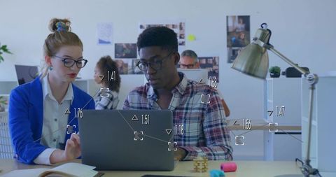 Young professionals collaborating over laptop with data overlays in modern open office