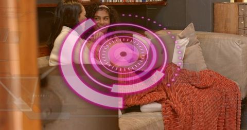 Two friends sharing laptop on cozy beige couch with magenta HUD overlay, living room