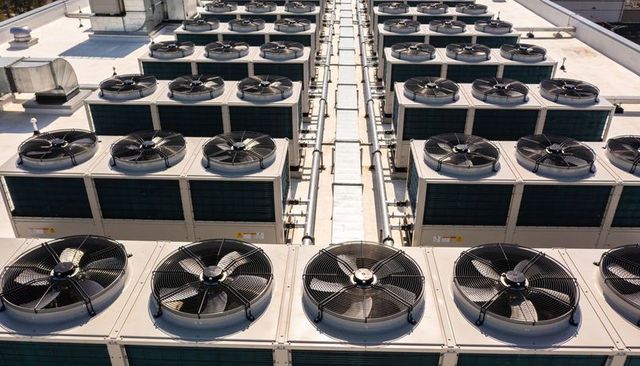 Rooftop hvac condenser units lining service walkway with axial fans and piping
