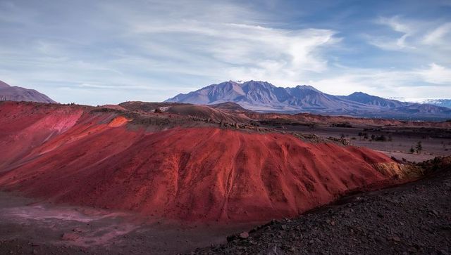 Vivid red badlands revealing eroded gullies on arid plateau with distant mountains