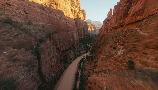 Revealing red-rock canyon corridor narrowing toward distant mesas over winding dry creek