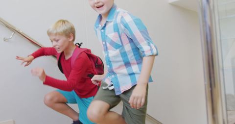 Two enthusiastic boys energetically ascend stairs, likely heading to or from class. Their expressions exhibit joy and eagerness, highlighting a dynamic and energetic school atmosphere. Ideal for educational materials, children's activities, or back-to-school campaigns emphasizing playfulness and excitement in learning environments.