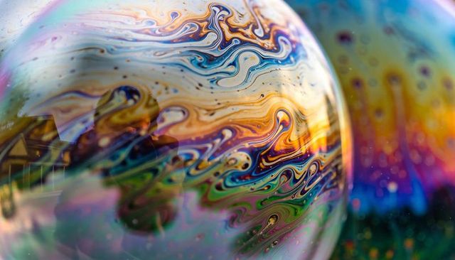 Iridescent soap bubble macro showing thin-film rainbow swirls at sunset