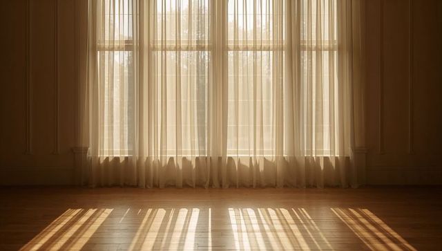 Sunlight filtering through sheer curtains casting warm stripes on hardwood floor