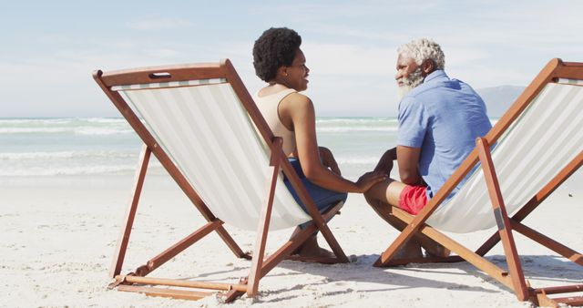 African american couple holding hands and lying on sunbeds on sunny beach. healthy and active time beach holiday.