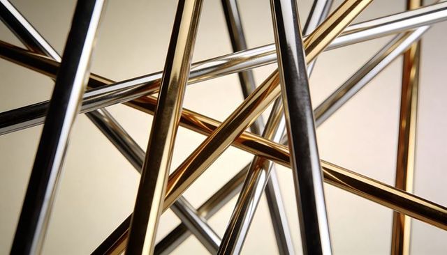 Intersecting polished gold and chrome rods creating abstract metallic lattice sculpture