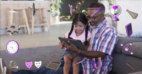 Grandfather teaching granddaughter on tablet with purple ar education icons, cozy home