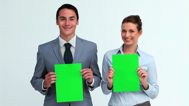 Two business professionals in formal attire holding blank green signs in a studio backdrop. The blank signs, often used for advertising and marketing campaigns, allow for customization. Ideal for digital content, promotions, and corporate designs.