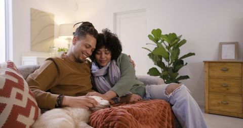 Couple cuddling on couch petting dog in cozy modern living room with warm decor