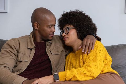 Couple cuddling on sofa wearing smartwatches sharing comfort and intimate moment at home