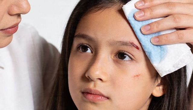 Caregiver applying cold compress to girl eyebrow after minor facial abrasion for home first aid