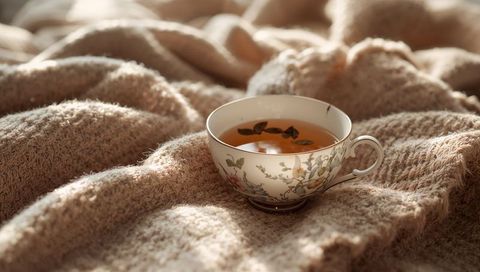 Porcelain teacup resting on cozy wool blanket with floral design and amber tea