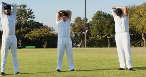 Cricket players stretching on grassy field before match wearing white uniforms