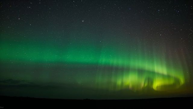 Dancing green aurora borealis stretching across starry night sky over dark horizon