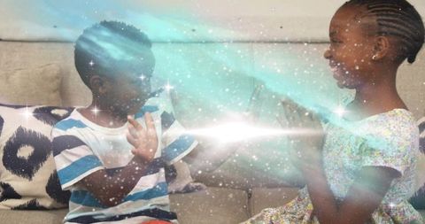 Joyful african-american siblings playing hand clapping game with sparkle effects