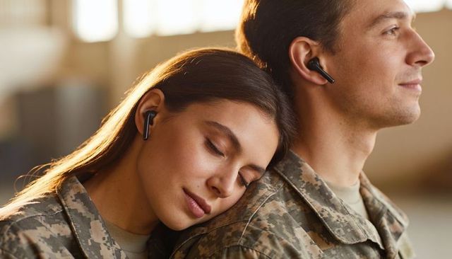 Young military couple sharing tender moment leaning in camouflage uniforms with earbuds