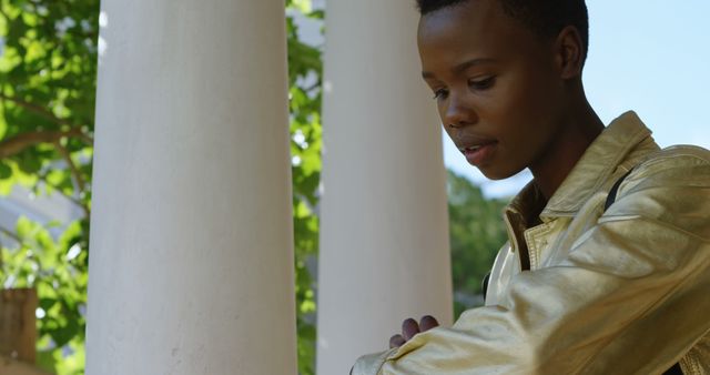 Young person wearing gold jacket standing near white columns and greenery - Download Free Stock Images Pikwizard.com