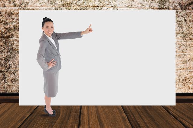 Businesswoman in professional attire pointing at blank billboard, ideal for corporate presentations, advertising, or promotional materials. The modern office background with wooden floor and stone wall adds a professional touch, making it suitable for various business contexts.