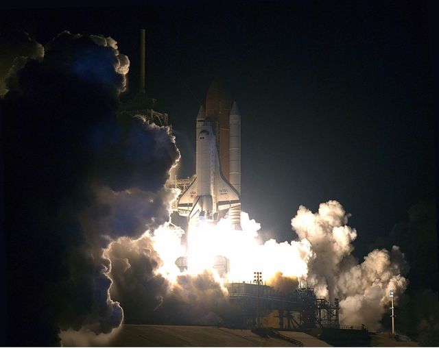 The image depicts night launch of Space Shuttle Atlantis on May 15, 1997, emphasizing its powerful thrust and dramatic lighting against dark sky. This historical event marks STS-84 mission, highlighted by the sixth docking between a Shuttle and Mir. Use this for educational materials, documentaries, articles on space exploration, and highlighting international collaborations in space.