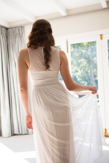 Rear view of young bride in wedding dress standing at home