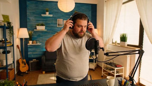 Male podcaster adjusting headphones recording podcast in cozy home studio with microphone