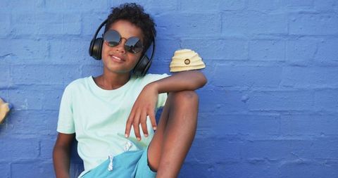 Stylish boy with headphones relaxing against blue brick wall
