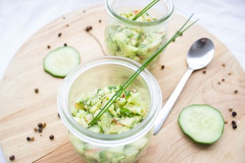 Serving cucumber avocado salsa in glass jars with chives on wooden board