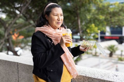 Senior woman enjoying healthy salad and fresh orange juice on urban terrace
